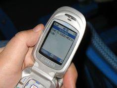 a person holding a silver cell phone in their hand and pressing buttons on the screen