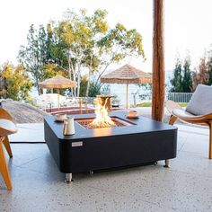 a fire pit sitting on top of a patio next to chairs and an umbrella over it