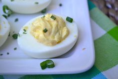 deviled eggs on a white plate with green garnishes and seasoning