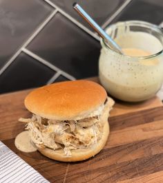 a sandwich on a wooden cutting board next to a glass of milk and a spoon