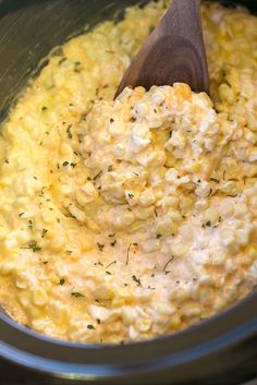 a wooden spoon mixing corn in a crock pot with some seasoning on top