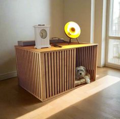 a dog is sitting in a wooden crate under a table with a clock on it