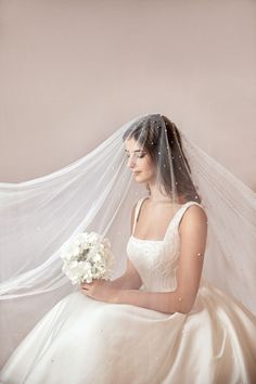 a woman wearing a wedding dress and veil holding a flower in her hand while sitting down