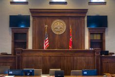 an empty courtroom with two laptops on the desk and three american flags hanging from the wall