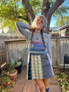 a woman standing in front of a tree with her hands on her head and wearing a skirt