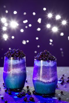 two glasses filled with purple and blue liquid sitting on top of a table next to each other