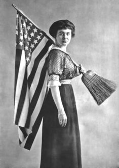 an old black and white photo of a woman with a flag on her shoulder holding a broom