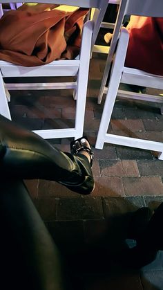 a pair of black shoes sitting on top of a brick floor next to two white chairs