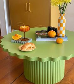 a green table topped with oranges and croissants next to a vase filled with flowers