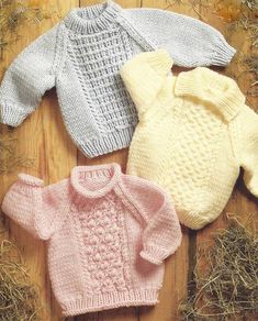 three knitted sweaters laid out on top of hay