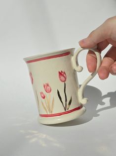 a hand is holding a coffee cup with flowers painted on the outside and red trimmings