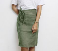 a woman standing in front of a white wall with her hands on her hips wearing a green skirt