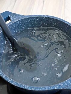 a blue pan filled with water on top of a wooden table next to a knife