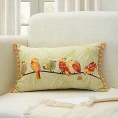 a white couch with a colorful pillow on top of it and two birds sitting on the branch