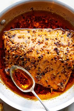 a pan filled with meat and sauce on top of a white countertop next to bread