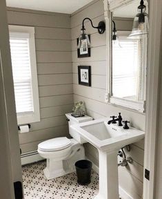 a white toilet sitting next to a sink in a bathroom under a mirror and light fixture