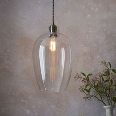 a clear glass light hanging from a ceiling fixture next to a vase with flowers in it