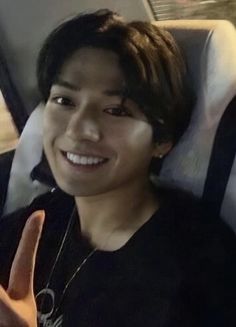 a young man sitting in the back seat of a car holding up a peace sign