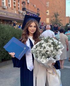 a woman in graduation gown holding a bouquet of flowers and a blue folder with writing on it