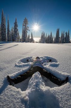 a person laying in the snow with their legs spread out to look at the sun