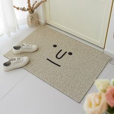 two pairs of shoes sitting on the floor next to a door mat with a smiley face drawn on it