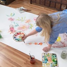 a girl is painting on the floor with watercolors