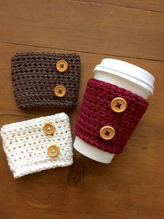 three crocheted coffee cozyies sitting on top of a wooden table