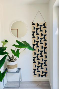 a plant in a pot next to a wall hanging with circles on it and a round mirror