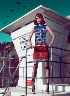 a woman standing on top of a boat next to a lifeguard tower with her hand on the railing