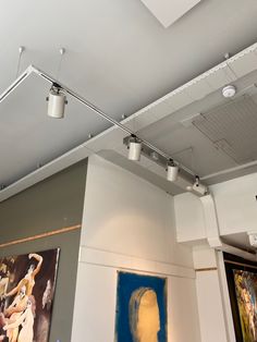 an art gallery with paintings on the wall and ceiling lights hanging from the rafters