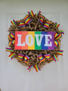 a wreath with the word love painted on it and rainbow ribbons hanging from it's front door