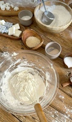 a wooden table topped with bowls and whisks filled with flour next to measuring spoons