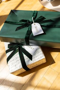 two wrapped presents sitting on top of a wooden floor next to each other, tied with green ribbon