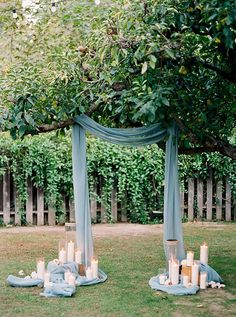 an outdoor ceremony setup with candles and blue draping on the grass, surrounded by greenery