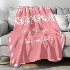 a pink blanket with the words we love you momma on it in white lettering, sitting on a grey couch