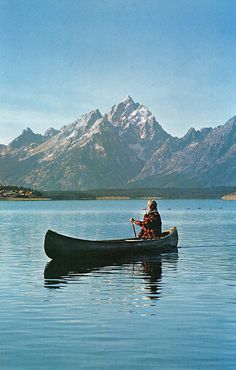 a person in a canoe on the water with mountains in the background