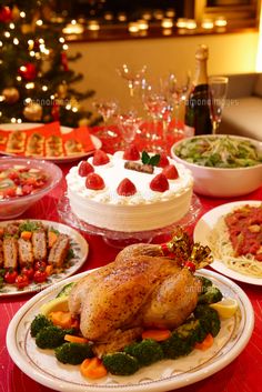 a table full of food with plates and bowls on it, next to a christmas tree