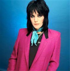 a woman with black hair wearing a pink suit and blue scarf, posing for the camera