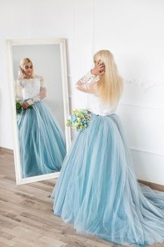 a woman standing in front of a mirror wearing a long blue skirt and white top