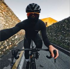 a man riding a bike down a street next to a stone wall and wearing a helmet