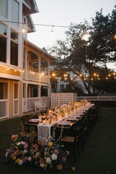 a long table is set up outside at night with lights strung from the ceiling and flowers on the tables