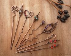 several different types of earrings on a wooden table next to dried berries and twigs with leaves