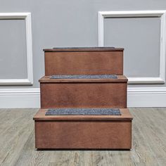 three brown boxes sitting on top of each other in front of a white wall and wooden floor