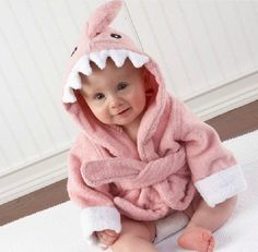 a baby wearing a pink shark robe on top of a white rug in front of a wall