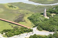 an aerial view of a lighthouse and road in the middle of green fields with trees