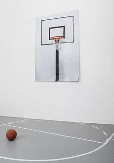 a black and white photo of a basketball in the middle of a gym with a hoop hanging on the wall