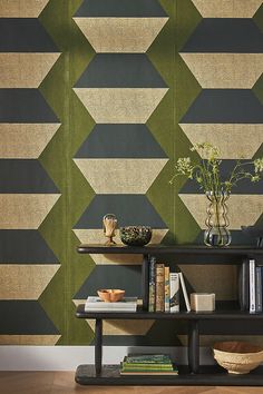 a book shelf with books and vases on it in front of a geometric wallpaper