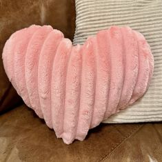 a pink heart shaped pillow sitting on top of a brown couch