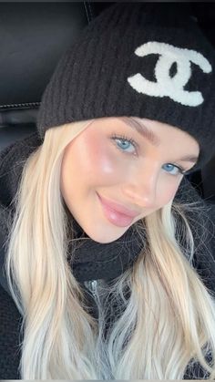 a woman with blonde hair wearing a black beanie and smiling at the camera while sitting in a car