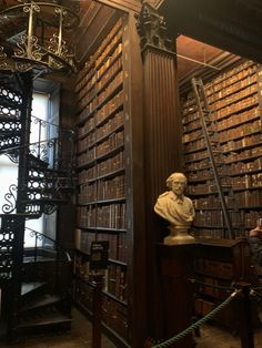 an old library filled with lots of books next to a busturine and spiral staircase